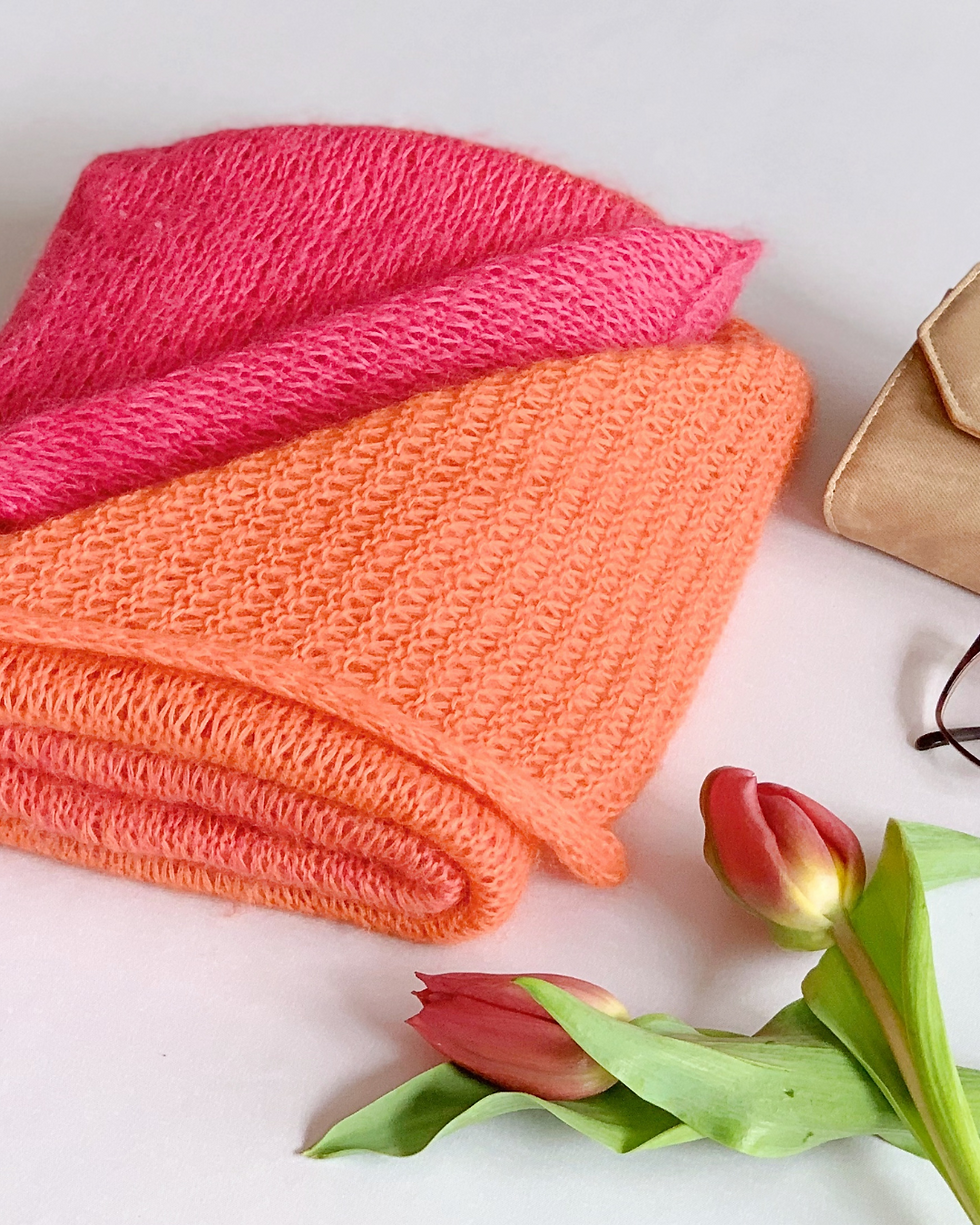 Miniaturbild: Gefaltete rosa und orangefarbene Textilien mit beiger Tasche, Brille und zwei rosa Tulpen.