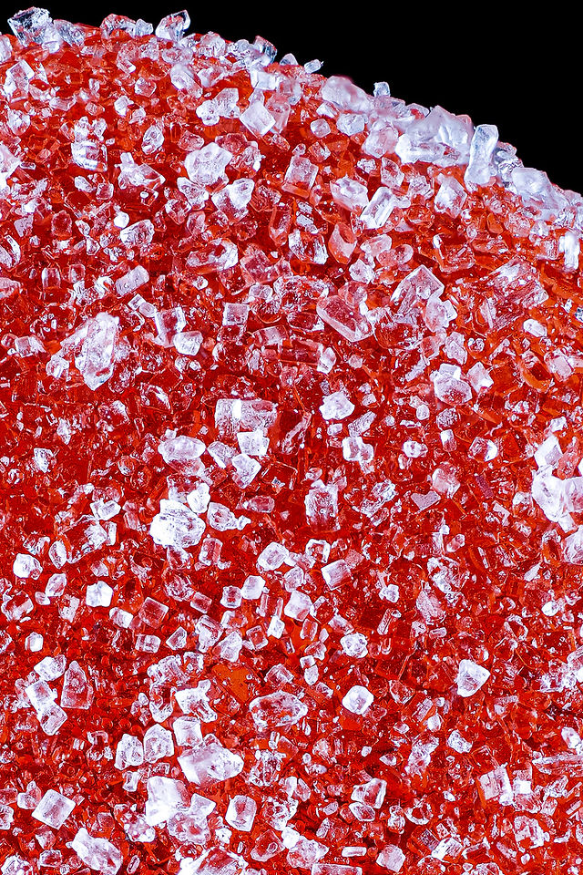 A professional high-fidelity studio product photograph of a Do Drops cannabis-infused gummy package centered against a clean white background. In the foreground, a pile of translucent, sugar-coated gummies is displayed in sharp macro focus, showcasing the detailed crystalline texture of the sugar coating and the vibrant color of the fruit-flavored edibles.