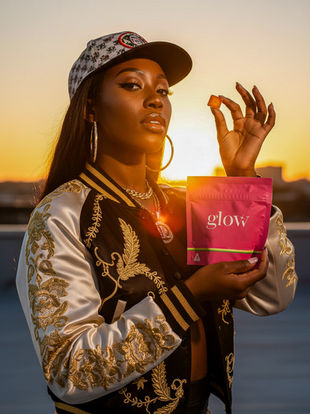Model in streetwear cap and gold jacket holding Glow Watermelon Blush gummy to the sun, golden hour cannabis photography Maryland
