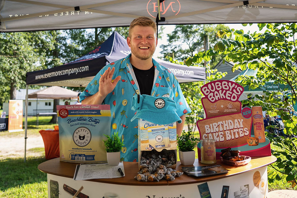 A smiling brand rep waves from behind the Bubby’s Baked booth, surrounded by cannabis edibles and birthday cake bites at ShoreFest.
