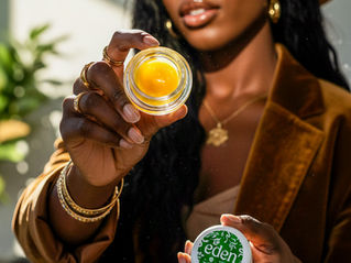 A woman in a brown suit and wide-brim hat holding up a jar of bright yellow Eden solventless rosin toward the camera.