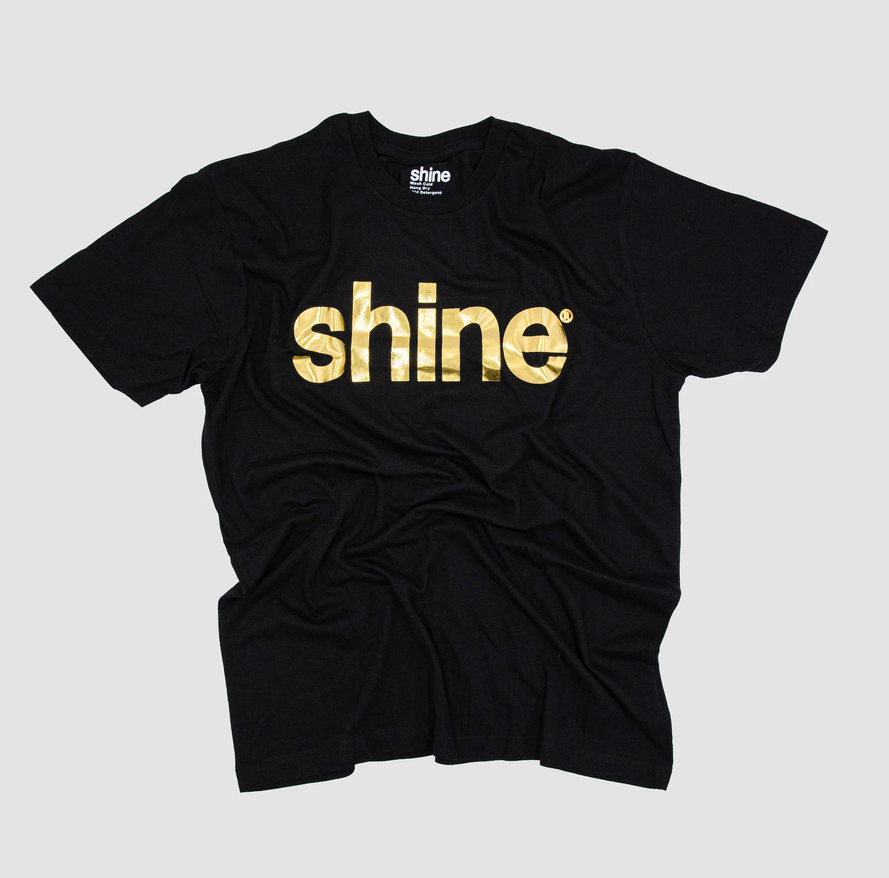 A black t-shirt featuring the word "shine" in bold, gold letters across the chest. The gold lettering gives the shirt a sleek, luxurious look that stands out against the dark fabric.