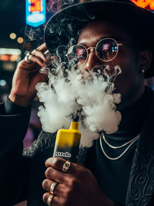 A man in a black hat and round glasses exhales thick vapor while holding a yellow Strane vape, lit by neon signs in a nighttime city environment.