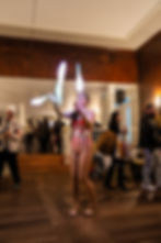 A female performer in a red and white striped circus outfit juggles illuminated glowing clubs in the middle of the dance floor.