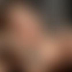 A woman with bold makeup and gold jewelry poses with Curio Wellness OG Kush Breath, holding a lit joint above a marble table covered with premium cannabis buds.