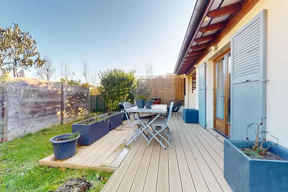 Terrasse en bois clair avec table et chaises pliantes bleues. Jardinières anthracite et barbecue. Persiennes bleues fermées sur porte-fenêtre double. Colocation Arborea à Viry.