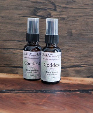 Goddess Face Serum.jpg a picture of two amber bottles with small pump sitting on wood stand