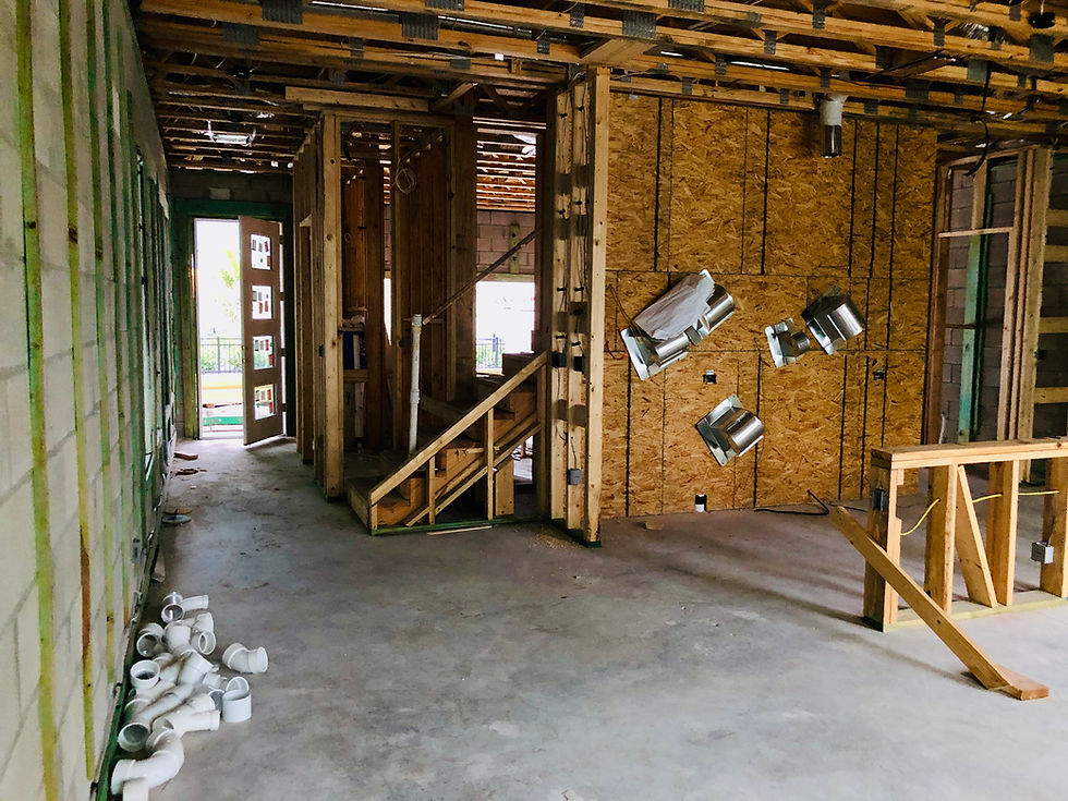 Unfinished building interior with exposed wooden frames, scattered pipes, and tools. Open doorway leads outside. Mood is industrial.