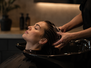 A client receives a restorative hair treatment at a black shampoo basin, representing professional bond-building treatments for stronger, healthier hair at Salon Ethos in Midtown Miami.