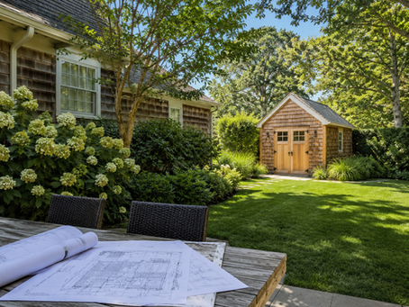 Traditional East Hampton backyard with a cedar shed, landscaped lawn, and property plans displayed on an outdoor table.