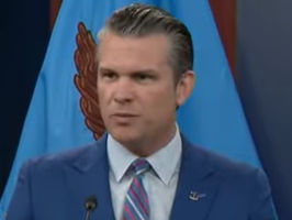 Pete Hegseth in a blue suit speaks at a podium with the Department of Defense seal. Blue flags and an American flag are in the background.