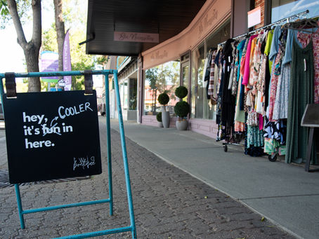 A sign outside a boutique shopping store downtown Camrose that says "hey, it's COOLER in here."