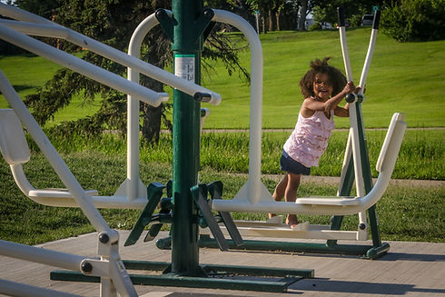 Little girl smiles as she uses the outdoor gym equipment in Jubilee Park.