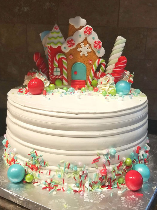 Christmas cake with white buttercream, topped with a gingerbread house, candy canes, lollipops, Christmas candies, and sprinkles around the base.
