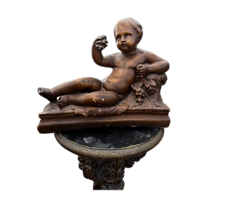 A statue of a cherub sitting on a rock, holding a grape in one hand, exuding a serene and playful demeanor.