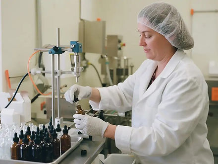 A technician in a hairnet filling and capping amber dropper bottles