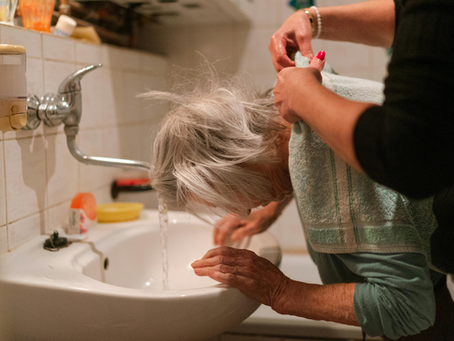 A caregiver helping an elderly woman wash her hair in a sink