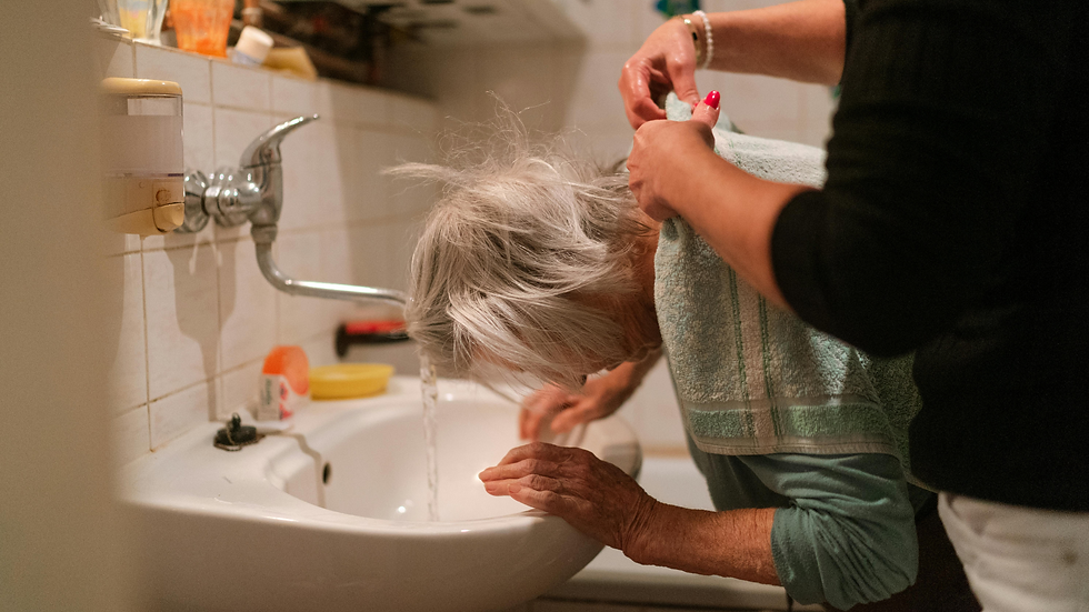 a caregiver helping an elderly woman wash her hair in sink
