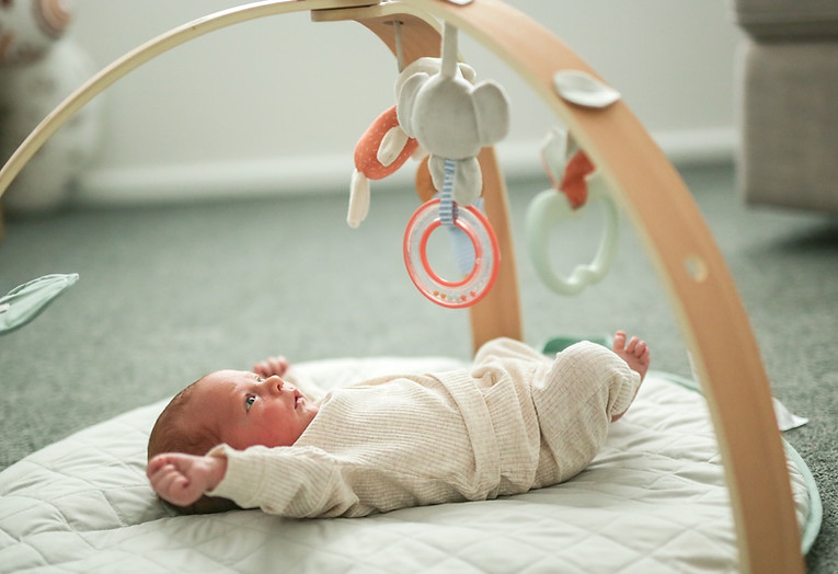 Newborn baby laying on the floor under a toy mobile in their nursery during a Noosa in-home lifestyle photography session.