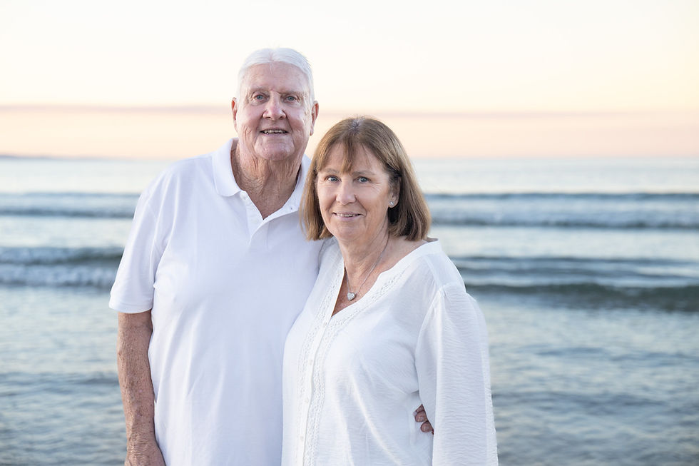Portrait of a grandmother and grandfather smiling at the camera on the beach at twilight, celebrating a milestone 70th birthday session with Noosa Family Photography.