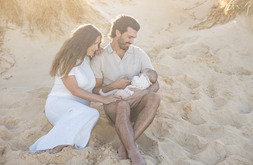 Parents sitting on a Noosa beach with their two month old baby backlit by the golden sunset light.