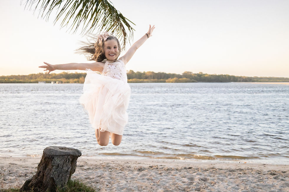 A young girl jumping from a rock under a palm tree into the calm waters of Noosa River at sunset, Noosaville family photography.