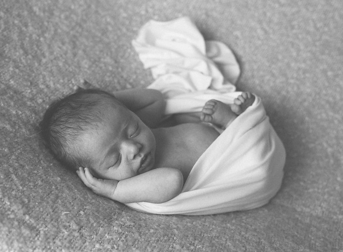 Close-up detail photograph of a newborn baby in a white wrap laying on a soft blanket during a Noosa lifestyle photo session