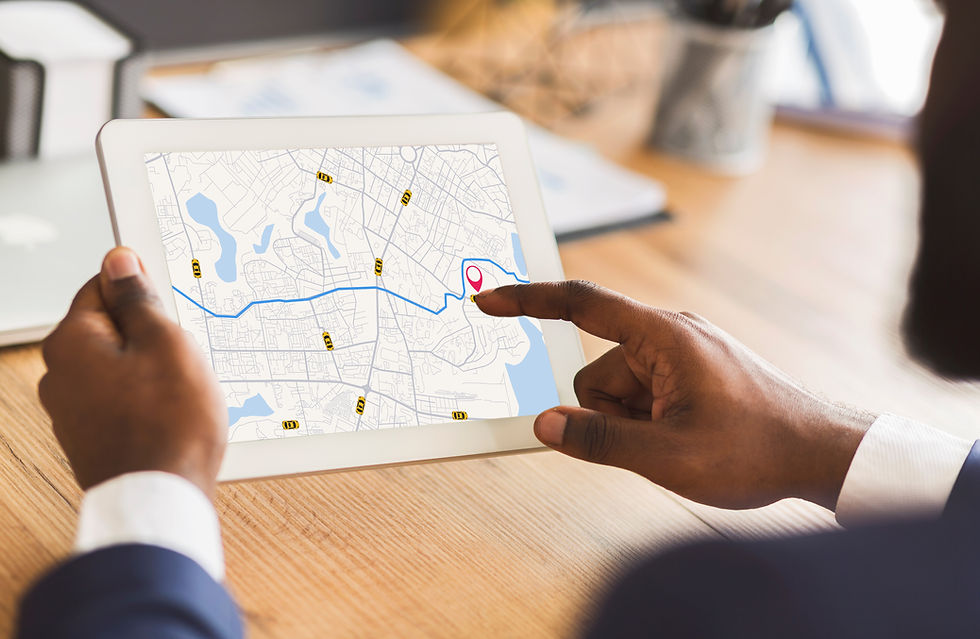 Hands holding a tablet displaying a map with a highlighted route and location pin. Office desk background with a pen holder. NEMT