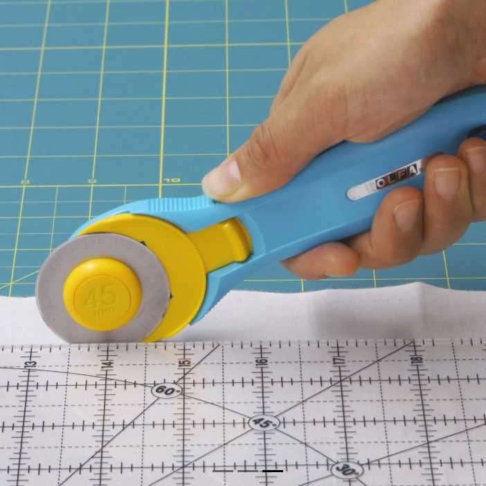 turquoise rotary cutter cutting fabric with rule
