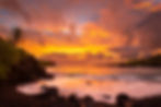 Orange sunset over waves breaking against a rocky shoreline in Hana, Maui, Hawaii.