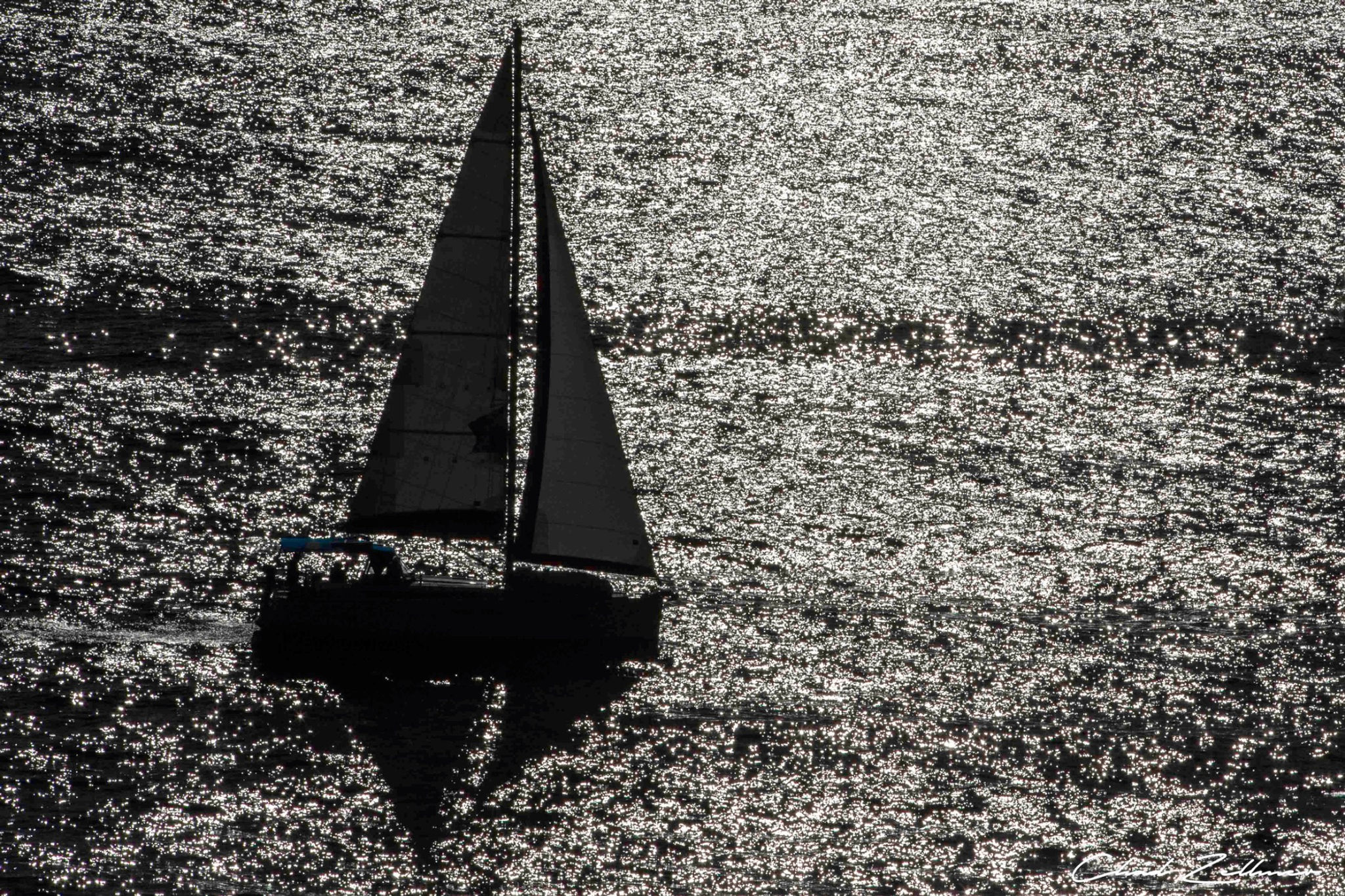 A sailboat appears in dark silhouette against sunlight sparkling across textured water.