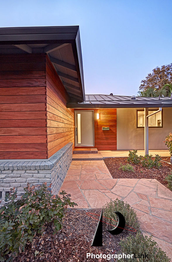 Modern ranch home with wood siding, metal roof, stone base, flagstone entry path, landscaped front yard, and covered entryway.