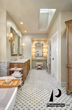 Luxury bathroom with marble floor, wood vanity, double mirrors, and overhead skylight
