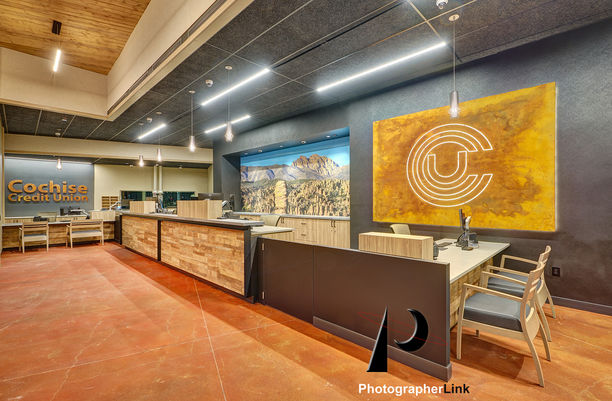 Contemporary Cochise Credit Union lobby featuring wood-accented teller counters, mountain mural, statement CU logo art, pendant lights, and open workspace