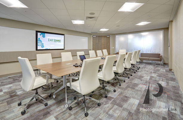Professional conference room with white swivel chairs, large wooden table, presentation screen, and bright lighting.