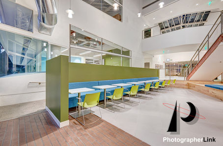 Contemporary office cafeteria featuring blue booth seating, green accent wall, white tables, lime green chairs, and open architectural design