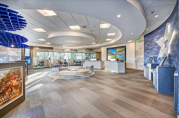 Modern financial office lobby featuring curved white seating, digital self-service kiosks, circular lighting, and large windows

