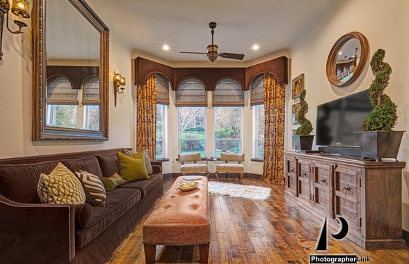 Elegant living room with brown velvet sofa, tufted bench, bay windows, modern chandelier, and wood floors
