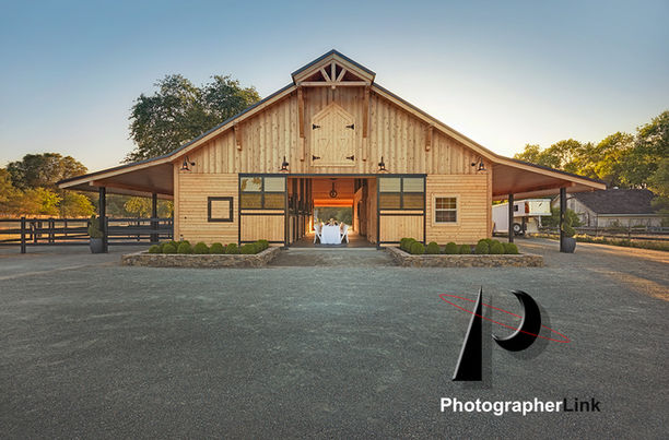 Contemporary wooden barn with light siding, landscaped entrances, large overhangs, and trees in a sunrise setting.