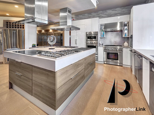 Modern kitchen with central island, gas cooktop, wood cabinets, stainless steel appliances, double ovens, and bright designer lighting.