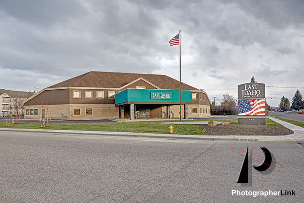 Exterior of East Idaho Credit Union building with tall flagpole, prominent signage, maintained lawn, and a dramatic sky.