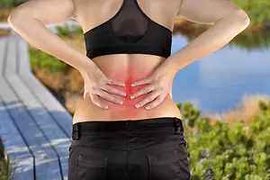 Back pain. Athletic woman in black sportswear standing and rubbing the muscles of her lowe