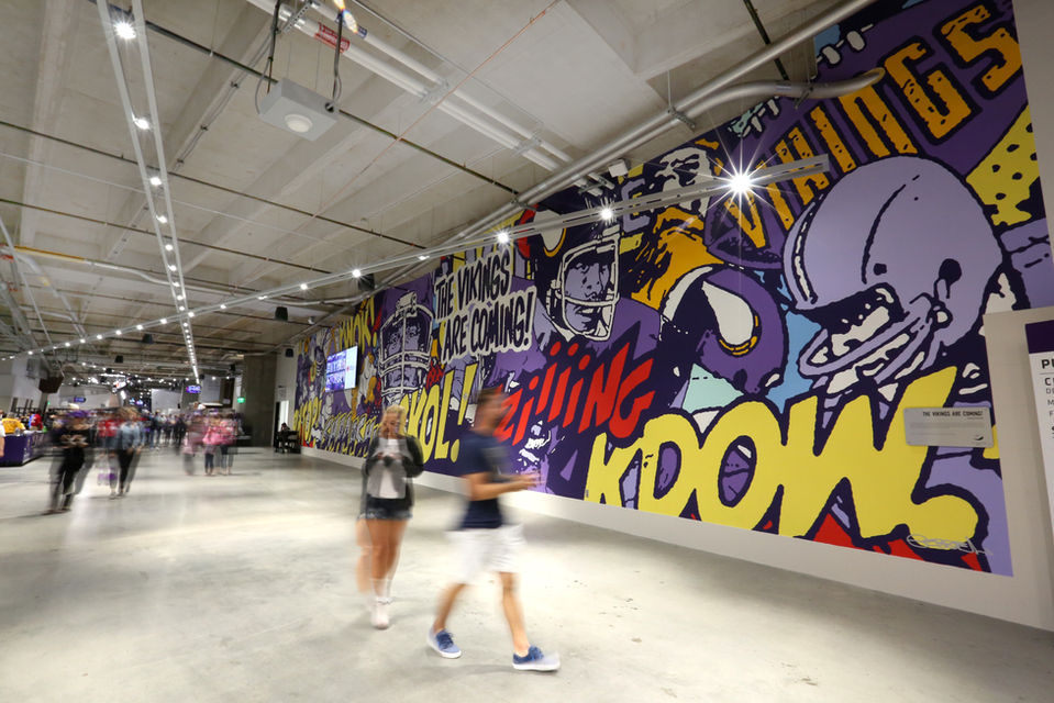 People walking by a mural wall highlighting Minnesota Vikings culture at US Bank Stadium