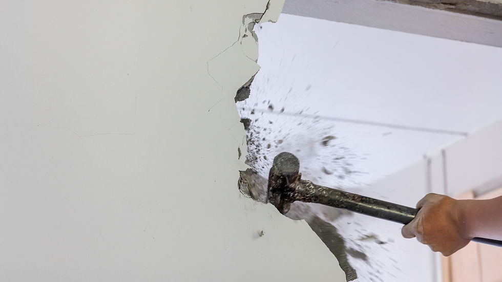 Hand using sledgehammer demolishing a wall; Interior Demolition shows construction work in progress
