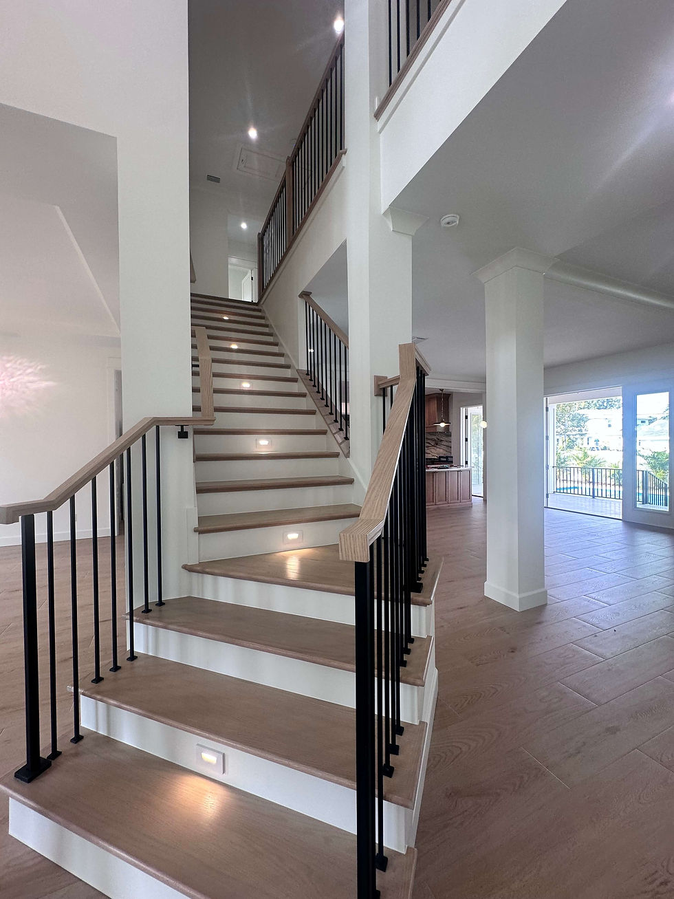 Modern staircase with wooden steps and black railings, lit by small floor lights. Open space with large windows and minimal decor.