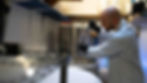 man in lab coat and gloves stirring fermenter of kombucha