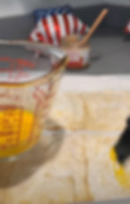 A clear pyrex measuring cup holds egg wash that is being brushed onto raw rectangles of puff pastry