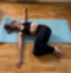 woman lying on yoga mat in supine twist position with arms outstretched at shoulder height and knees on the floor over to the right