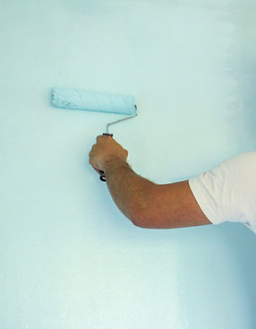 A person in a white shirt uses a paint roller to apply light blue paint on a wall