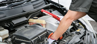 A mechanic checks under a car hood, using a red flashlight